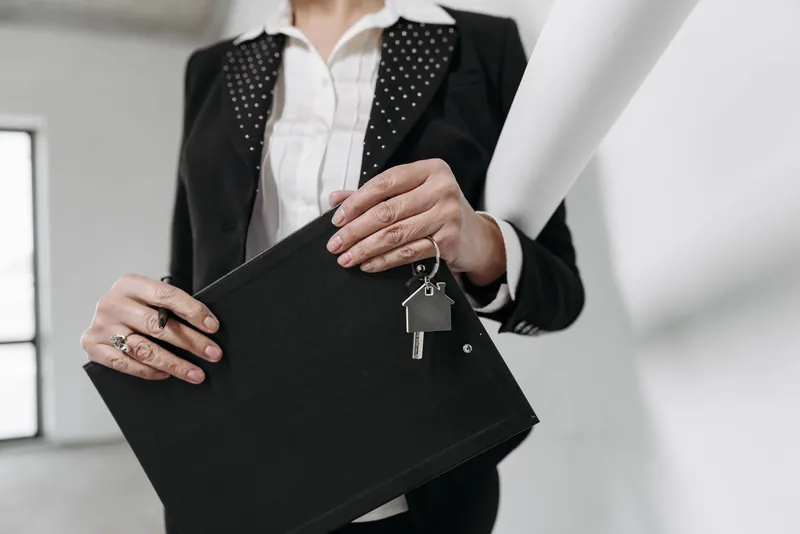 En person i dress holder en svart mappe med en husformet nokkelring hengende fra kanten
